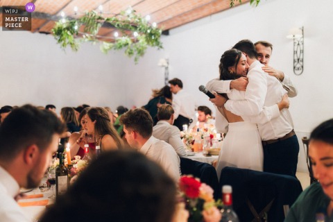 At Château de Campet in Landes, France, the newlyweds embrace the groom’s younger brother after his speech during the wedding meal, sharing a heartfelt family moment.