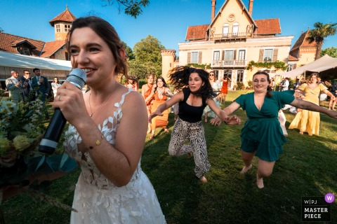 At Chateau du Prada in Saint-Lon-les-Mines, France, wedding guests eagerly reach for the bouquet during the toss, creating a playful, sports-like action scene on the lawn.