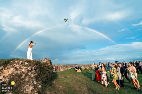 At Fort la Prée on Île de Ré, France, the bride prepares to toss her bouquet as excited wedding guests gather for the traditional bouquet throw.