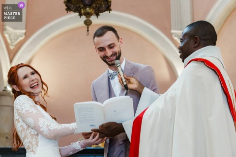 At the church, the newlywed couple shares a burst of laughter during a reading, capturing a joyful and lighthearted moment of their wedding ceremony.