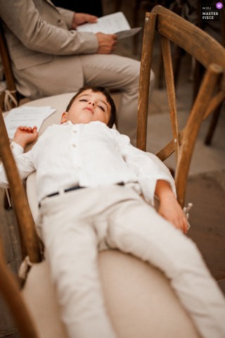 At Burningfold Barn in Godalming, UK, the page boy naps during the wedding ceremony, stretched out across several chairs, adding a sweet and candid moment to the day.