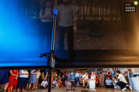 During the reception at Château de Beauséjour, the couple and their guests watch an emotional video projection of the wedding, the light from the screen illuminating their faces.