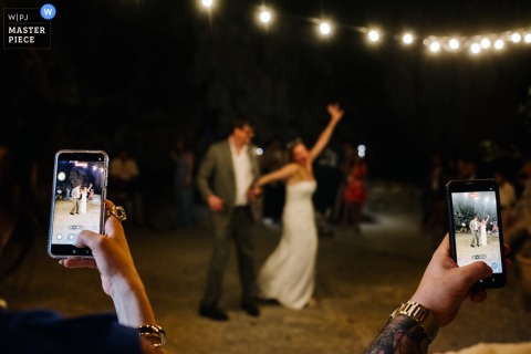 At Tonnara di Scopello, guests hold up their phones to capture the couple’s first dance at night, their screens glowing around the newlyweds.