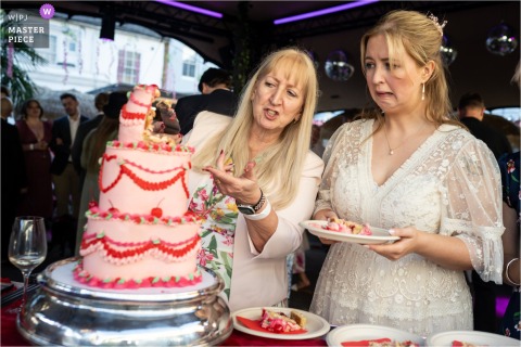At The Pig and Whistle pub in Hertford, the bride and her mum puzzle over cutting a leaning cake in the heat, sharing a lighthearted moment together. 