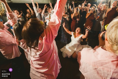 At Anglers Rest in Dublin, the bride sits on the dance floor in front of a lively crowd, joining in the fun during a Sing Along Social at her wedding.