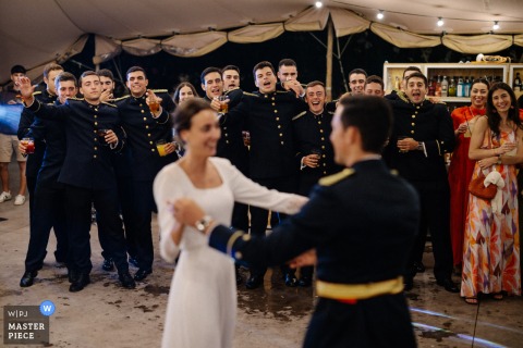 At Torre de Mirahuerta wedding venue in Zaragoza, Spain, the groom dances with the bride while many friends in military uniforms watch, creating a striking scene filled with camaraderie and celebration.