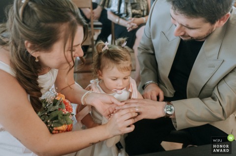 An intimate scene unfolds at Montmanoir, France, as the couple exchanges wedding rings while a little girl looks on, adding innocence and sweetness to the ceremony.