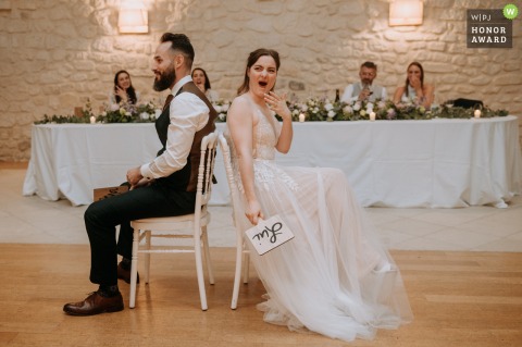 At Le Clos Barisseuse in France, the bride is visibly shocked during a wedding game, surrounded by guests who eagerly share in the surprising moment.