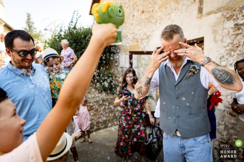 At City Hall in Reventin Vaugris, Isère, France, the groom is playfully showered with soap bubbles in his eyes, adding a whimsical and painful touch to the special day.