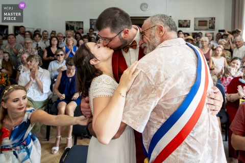 At Mairie de Mens, Isère, the mayor embraces his son and new daughter-in-law at the end of the civil ceremony in a moving family moment.