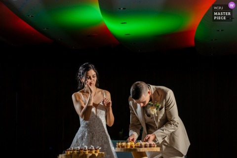 At the Dolder Grand in Zürich, the groom works on cutting a slice of cake while the bride licks her fingers, sharing sweet wedding traditions.