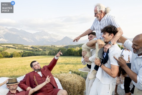 At La Maison-Ateliers in Cornillon-en-Trièves, Isère, the groom’s grandfather is joyfully lifted on the guests’ shoulders, celebrating family and generational connections at the wedding.