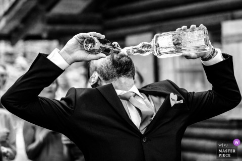 At the wedding party, a man pours both beer and aims into his mouth simultaneously. Captured in black and white, the shot exudes playful energy.