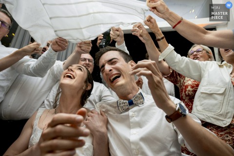 At Domaine des Cèdres in Villebois, Ain, the bride and groom participate in the “Vivat Flamand,” being joyfully sprayed with champagne through a cloth—a lively Flemish wedding tradition.