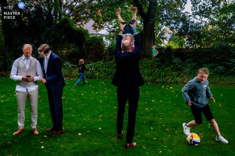 At Weingut Hahn in Alzey, male guests enjoy the outdoor reception, laughing and playing with kids on the grass in the afternoon light.
