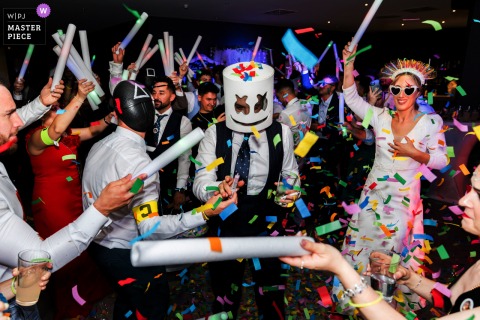 At Hotel HO Jaén in Jaén, Spain, the wedding party turns wild with guests donning crazy masks and dancing through a shower of confetti, capturing the joyful and lively spirit of the reception celebration.