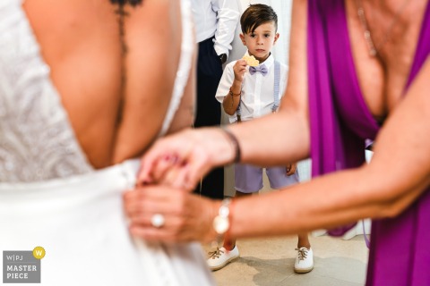 At the bride’s house in Montilla, Córdoba, Spain, a boy’s curious gaze steals the scene as he watches the dress being buttoned up. He’s in sharp focus behind, framed artfully by the bride’s dress back and helping hands.