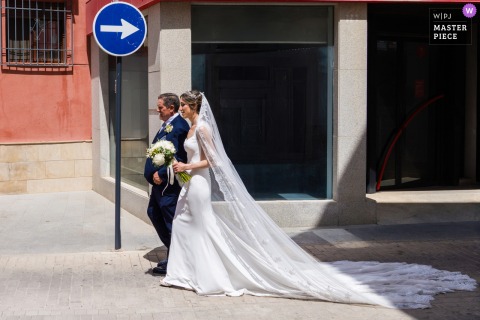 In Rus, Jaén, Spain, the bride and groom walk hand in hand through the urban streets, while a traffic sign humorously points in the opposite direction, capturing a playful wedding play on going your own way.