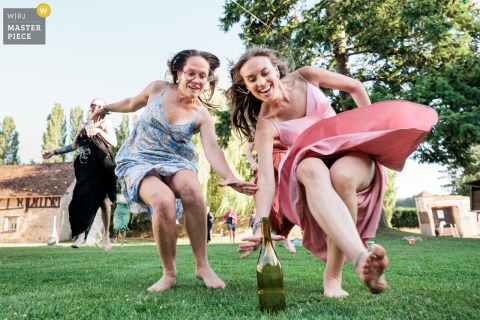 At a reception venue in Versailles, Yvelines, bridesmaids dash across the grass, racing to catch a bottle, capturing a playful and spirited moment of friendly competition during the wedding festivities.