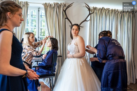 Playful Antler Illusion During Bridal Prep At Chateau De Boucq France At Chateau de Boucq, France, the bride gets ready for her big day with a touch of humor—an antique wall-mounted head rack behind her creates the playful illusion of antlers, adding a lighthearted moment to her preparations.