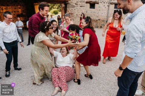 At Domaine des Monts du Lyonnais in Rhône, the bouquet toss ends with a guest landing on the ground, capturing a playful and lighthearted moment of laughter and surprise during the celebration.