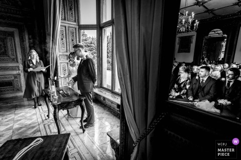 At Manor by the Lake in Cheltenham, UK, the couple participates in a Filipino candle ceremony as seated guests watch. The large mirror behind them captures the reflections of all, adding depth and cultural richness to this meaningful moment.
