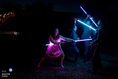 At Fort Wellington National Historic Site, wedding guests playfully wield lightsabers, pretending to stab the groom as an onlooker points, bringing a fun, Star Wars-inspired energy to the celebration and sparking laughter all around.