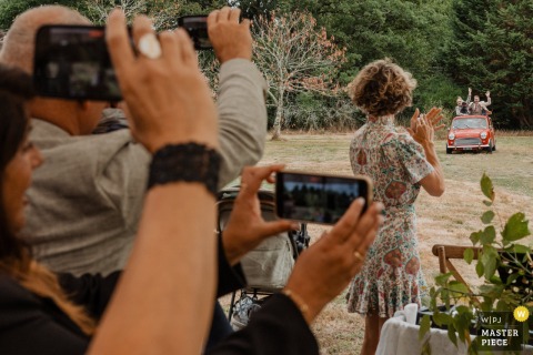 At Gîte de la Maronnière in Nantes, France, the newlyweds arrive in a small red car while all their guests enthusiastically capture the moment on their phones, creating a vibrant and unforgettable wedding entrance.