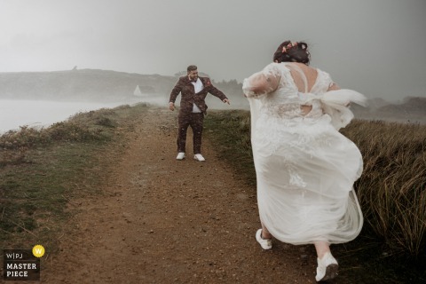 At the Church of Ploeven in France, the bride and groom run together through driving, horizontal rain with movement and laughter despite the stormy weather.