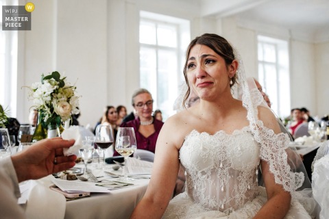 At Grand Hotel du Pont in Le Pont, Switzerland, the bride’s face shows deep emotion as she listens to a heartfelt speech. Someone gently hands her a tissue, capturing a touching and sincere moment during the celebration.