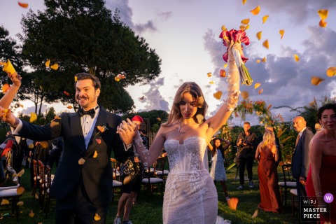 At Kemer Country Hotel in Göktürk, Istanbul, Türkiye, the bride and groom walk down the aisle while guests gather around them, celebrating and showering the couple with rose petals, capturing a joyful and festive moment.