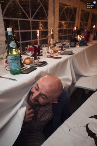 At Serezin de la Tour in Isère, Auvergne-Rhône-Alpes, France, laughter bursts out from beneath the tablecloths as unexpected games unfold during the wedding dinner, capturing the fun and spontaneity of the celebration.