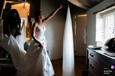Bride’s Veil And Train Adjusted On Stairs At Bury Court Hampshire At Bury Court in Hampshire, the bride reaches for her veil while someone lifts her train as she ascends the small stairs, highlighting a graceful and intimate wedding day moment.