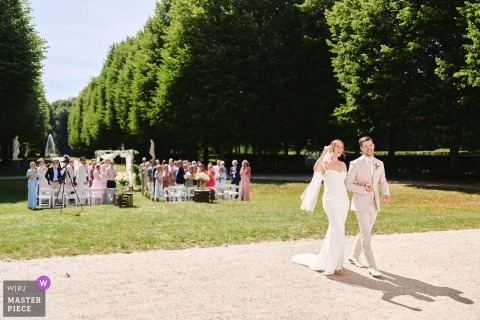 In Amsterdam, Noord Holland, the newly married couple beams with happiness as they walk away from their grass lawn ceremony onto a gravel path, capturing the joyful transition into their new life together.
