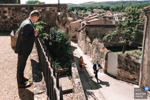 At the Church of Saint-Saturnin in France, the groom anxiously watches as the much-anticipated late arrival finally reaches the church, capturing a moment filled with suspense and relief before the ceremony begins.
