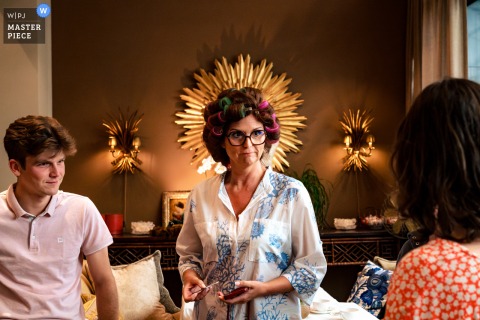 In the hotel lounge of Brabant Wallon, Wallonie, the bride stands elegantly with a decorative crown displayed on the wall behind her, creating the effect of a regal silhouette in this striking wedding day scene.