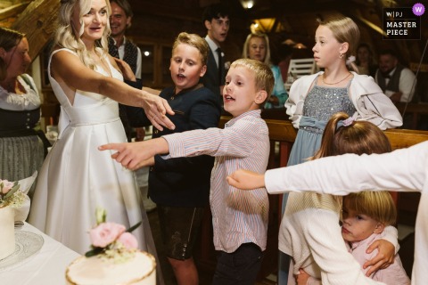 At Freiseder in Austria, the bride playfully bargains with eager kids for a slice of cake before it’s even cut, capturing the fun and lively spirit of the reception.