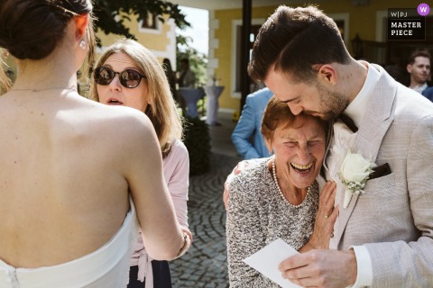 At Firlingerhof in Scharten, Austria, a genuine moment unfolds as the groom receives a warm hug from his grandmother in the sunshine during the reception, capturing generational love and heartfelt connection.