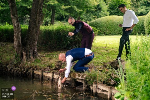 At a reception venue in Brabant Wallon, Wallonie, the groom adds a twist to the celebration by catching a fish from the small lake, creating a spontaneous and memorable moment during the wedding festivities.