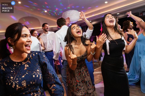At a reception venue in San Francisco, California, three women passionately sing along on the dance floor, capturing the energy and excitement of a memorable celebration.