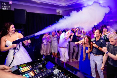 At Klooster Bethlehem in Haren, Groningen, Netherlands, the bride amps up the party by shooting a fog gun over excited guests beneath vibrant purple DJ lights, creating an energetic and unforgettable celebration atmosphere.