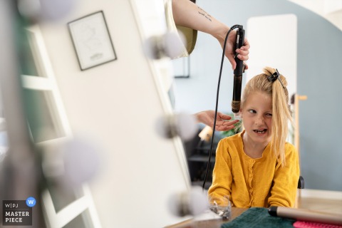In Zoetermeer, a playful scene unfolds as a girl makes a funny face while someone styles her hair. Reflections in the glass add depth and charm to this lighthearted moment with kids and creativity.