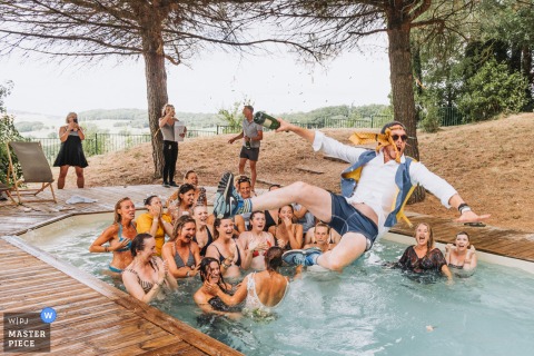At The Castelnau in Lectoure, France, the groom—still partially dressed in his wedding attire—leaps playfully into the pool to join guests already swimming, capturing spontaneous celebration and joyful energy.