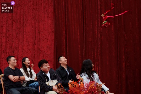 At a ceremony location in Taiyuan, Shanxi, the newlyweds toss the bouquet to their friends as it arcs overhead. The minimalist composition draws focus to the moment of anticipation in this elegant celebration.