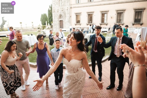 In the garden of Castello di Torre Alfina, Viterbo, the bride dances joyfully as guests form a lively circle around her. The scene is filled with celebration and the charm of an Italian castle wedding.