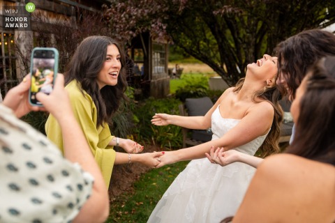 The Inn at Laureau Farm in Waitsfield, VT, offers a scene of joy as the bride laughs with friends during her wedding reception, surrounded by love and rustic charm.