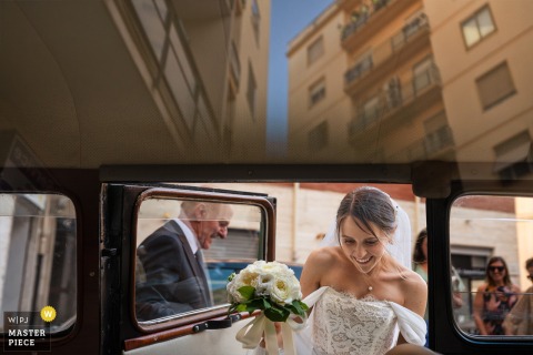 In Cagliari, Sardinia, the bride is framed in the car glass while leaving for the ceremony. Shadows and reflections reveal both her emotions and the scene unfolding behind the photographer.