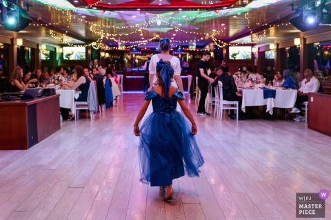 A whimsical moment in Istanbul, Turkey, as a young girl in a blue dress playfully mimics the bride, walking behind her across an empty dance floor. Captured from behind, the image radiates innocence and joy.