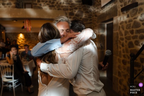 A heartfelt embrace shared indoors at Le Mas Girodier in Ardèche, as the bride hugs her father after his speech, dappled DJ lighting softly illuminating the emotional moment.
