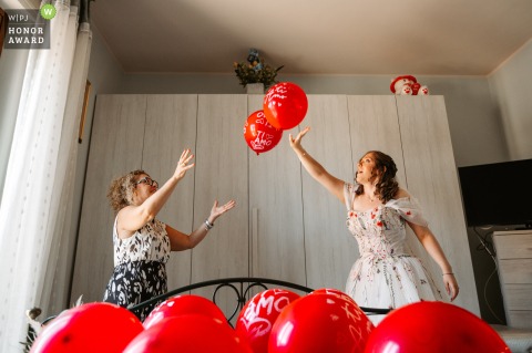 A Playful Game Unfolds As The Bride And Mother Toss Balloons Inside Their Home In Montefiascone Viterbo Italy Inside the bride’s home in Montefiascone, VT, a playful game unfolds as the bride and her mother toss balloons to each other that will later become part of the wedding decorations.